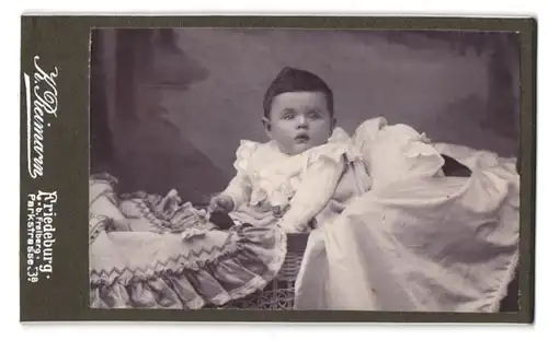 Fotografie K. Reimann, Friedeburg, Parkstrasse 53 B, Portrait niedliches Baby im weissen Kleid