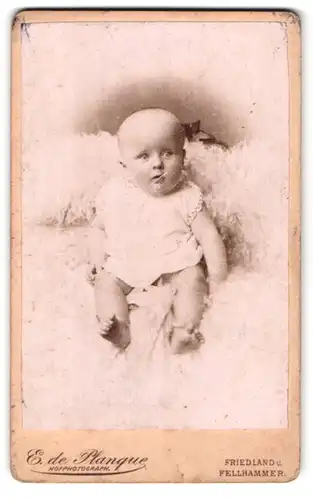 Fotografie E. de Planque, Friedland, Portrait süsses Baby im weissen Hemdchen auf Fell sitzend