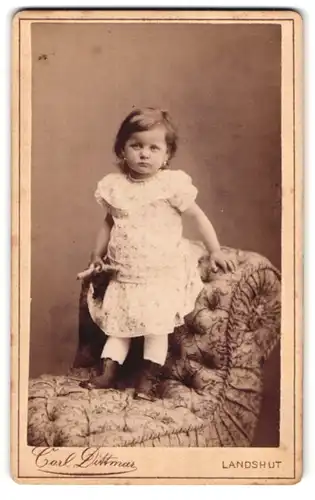 Fotografie Carl Dittmar, Landshut, Portrait niedliches kleines Mädchen im weissen Kleidchen mit Schnürrstiefeln