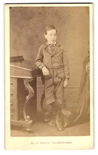 Fotografie London & County, London-EC, 63, St. Pauls Churchyard, Portrait kleiner Junge im Anzug an Pult gelehnt