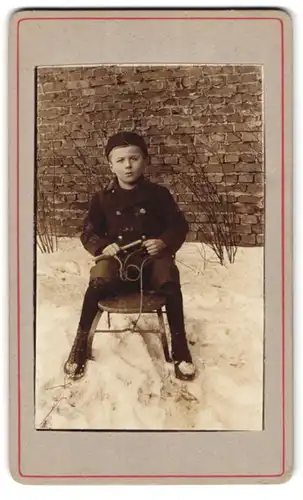 Fotografie unbekannter Fotograf und Ort, Portrait Bursche auf seinem Schlitten sitzend