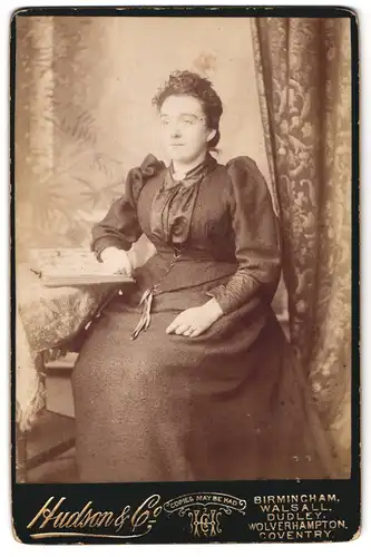 Fotografie Hudson & Co., Birmingham, Portrait bürgerliche Dame mit Album am Tisch sitzend