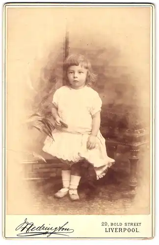 Fotografie Medrington, Liverpool, Bold Street 29, Kleines Mädchen in weissem Kleidchen steht neben Pflanze