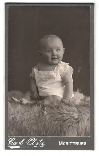 Fotografie Carl Platz, Moritzburg, Portrait süsses Kleinkind im weissen Kleidchen auf Fell sitzend