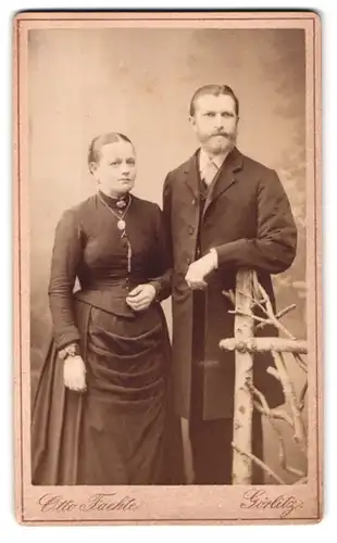 Fotografie Otto Faehte, Görlitz, Grüner Graben 29, Portrait elegant gekleidetes Paar am Holzzaun stehend