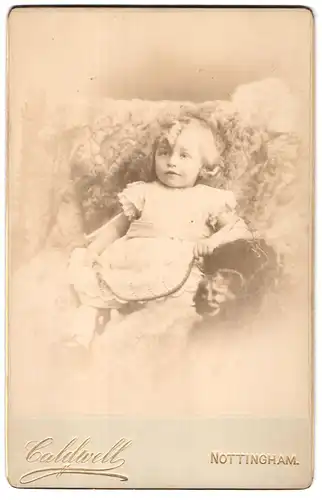 Fotografie G. Caldwell, Nottingham, Portrait kleines Mädchen im hübschen Kleid auf Fell sitzend