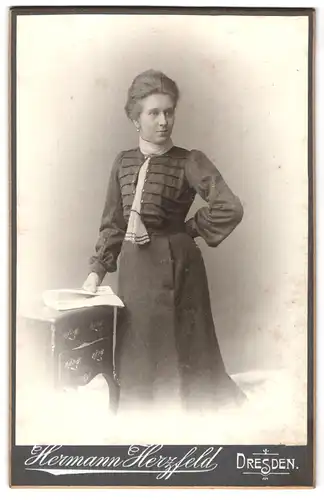 Fotografie Hermann Herzfeld, Dresden-A, Portrait bürgerliche Dame mit Zeitung an Kommode gelehnt