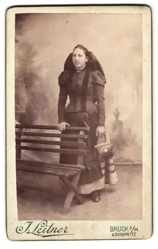 Fotografie J. Leitner, Bruck a. M., Hauptplatz 22, hübsche Dame mit Handtasche in regionaler Tracht