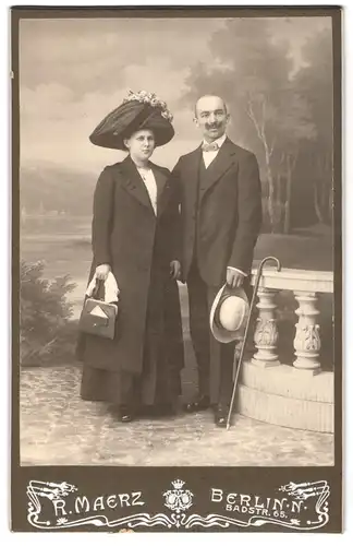 Fotografie A. Maerz, Berlin, Badstr. 65, elegantes Paar mit Hut vornehm gekleidet vor Kulisse im Foto-Atelier