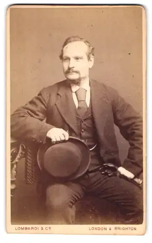 Fotografie Lombardi & Co., London, 113 Kings Road, Portrait stattlicher Herr mit Hut und Krawatte im Anzug