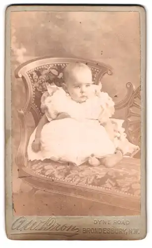 Fotografie A. W. Dron, Brondesbury, Dyne Road, Portrait Kleinkind im weissen Kleid sitzt auf einer Couch