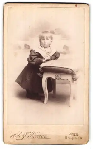 Fotografie Adolf Weiner, Wien, Landstrasse 114, Portrait niedliches Kleinkind im hübschen Kleid an Hocker gelehnt