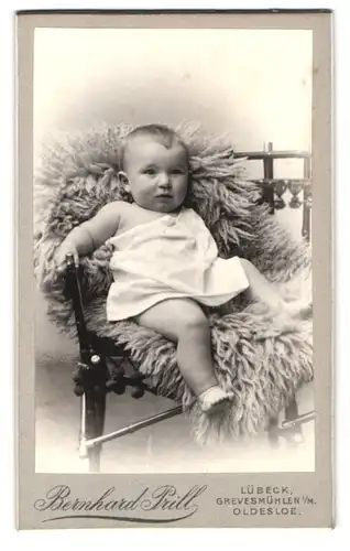 Fotografie Bernhard Prill, Lübeck, Breitestrasse 97, Portrait niedliches Kleinkind im weissen Hemd auf Fell sitzend