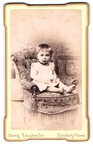 Fotografie Atelier Rauchmiller, Günzburg a / D., Portrait niedliches Kleinkind im weissen Hemd auf Sessel sitzend