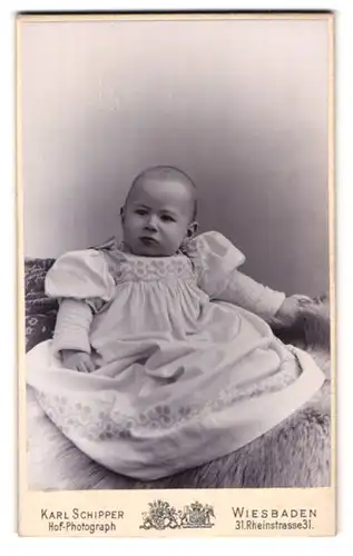 Fotografie Karl Schipper, Wiesbaden, Rheinstrasse 31, Portrait niedliches Kleinkind im hübschen Kleid auf Fell sitzend
