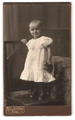 Fotografie Atlier Billström, Kiel, Holstenstrasse 43, Portrait kleines Mädchen im weissen Kleid mit Stofftier