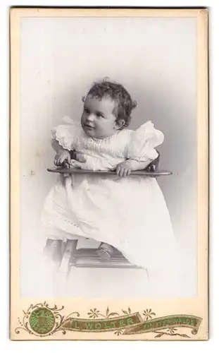 Fotografie L. Wolter, Finsterwalde, Schulstr., Portrait süsses kleines Mädchen im weissen Kleidchen im Kinderstuhl sitzend