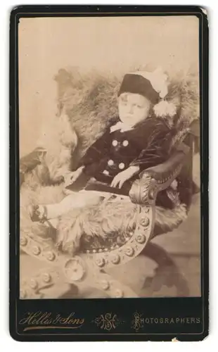 Fotografie Hellis & Sons, London, 211 & 213, Regent Street, Portrait niedliches Kleinkind im Mantel auf Fell sitzend