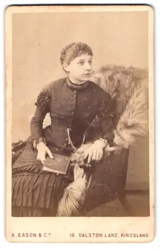 Fotografie A. Eason & Co., Kingsland, 16, Dalston Lane, Portrait bürgerliche Dame mit Buch auf Fell sitzend