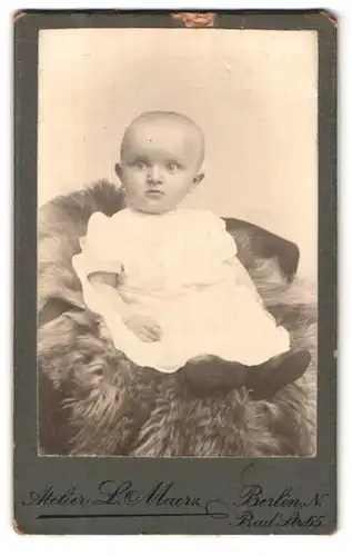 Fotografie L. Maerz, Berlin, Bad-Strasse 65, Portrait niedliches Kleinkind im weissen Kleid auf Fell sitzend