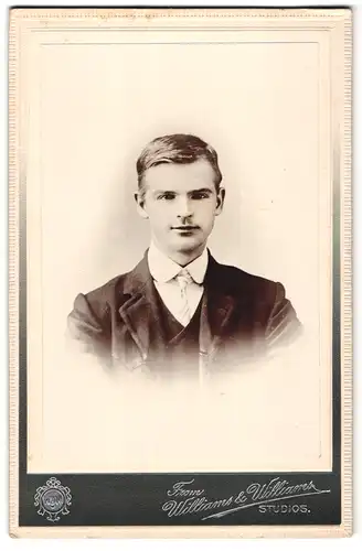 Fotografie Williams & Williams, Ort unbekannt, Portrait lächelnder Mann im Anzug