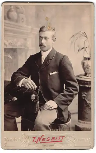 Fotografie T. Nesbitt, Blandford, Marketplace, Gut gekleideter Herr in gestreifter Hose sitzt rittlings auf Sessel
