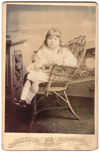 Fotografie A. & G. Taylor, Carlisle, Bank Street 18, Junges Mädchen in weissem Kleid sitzt auf geflochtenem Stuhl