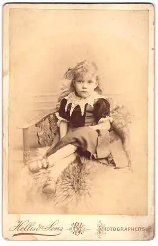 Fotografie Hellis & Sons, London, 211 & 213, Regent Street, Portrait kleines Mädchen im hübschen Kleid auf Fell sitzend