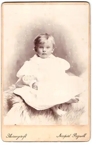 Fotografie Thorneycraft, Newport Pagnell, Portrait niedliches Kleinkind im weissen Kleid mit nackigen Füssen