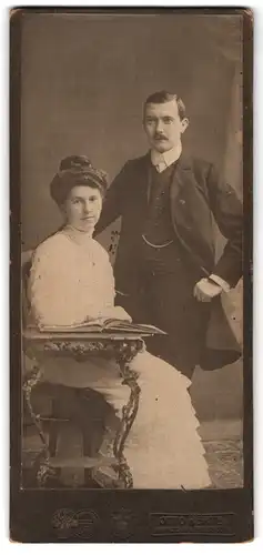 Fotografie Otto Hertel, Freiberg i / S., Portrait junges Paar in hübscher Kleidung mit einem Buch