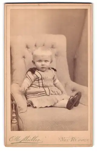 Fotografie Otto Müller, Neu-Ruppin, Paradeplatz 8, Portrait niedliches Kleinkind im hübschen Kleid auf Sessel sitzend