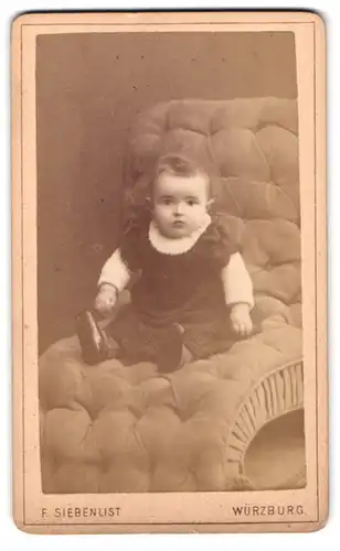 Fotografie F. Siebenlist, Würzburg, Portrait niedliches Kleinkind im Kleid auf Sessel sitzend