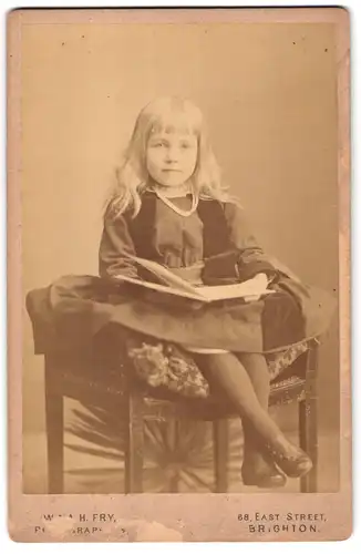 Fotografie W. and A. H. Fry, Brighton, 68, East Street, Portrait Mädchen im modischen Kleid mit Buch auf Hocker sitzend
