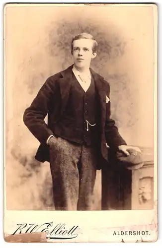 Fotografie R. W. Elliott, Aldershot, 93, High St., Portrait junger Mann in modischer Kleidung mit Schiebermütze