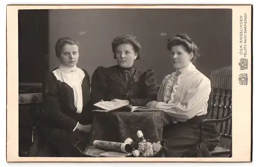 Fotografie Osk. Ensslinger, Darmstadt, Hügelstrasse 59, Portrait drei bürgerliche Damen mit Heft am Tisch sitzend