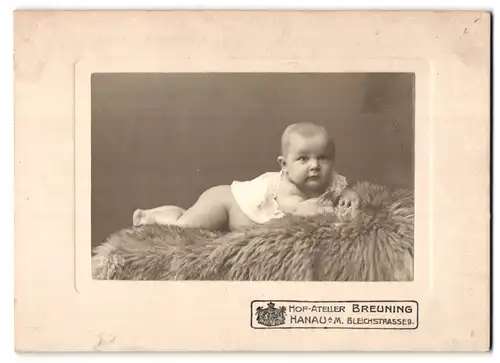 Fotografie Atelier Breuning, Hanau a. M., Bleichstrasse 9, Portrait niedliches Kleinkind im weissen Hemd auf Fell liegend