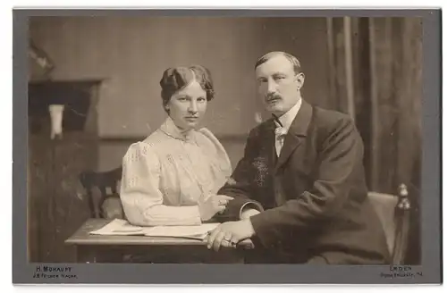 Fotografie H. Mohaupt, Emden, Grosse Bürckstrasse 74, Portrait bürgerliches Paar mit Heft am Tisch sitzend
