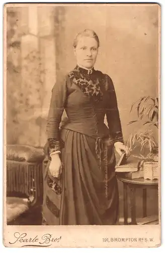 Fotografie Searle Bro`s, London-SW, 191, Brompton Road, Portrait bürgerliche Dame mit Büchern an Tisch gelehnt
