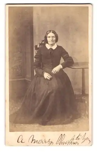 Fotografie unbekannter Fotograf und Ort, Portrait ältere Dame im Kleid am Tisch sitzend