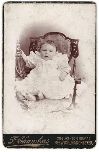 Fotografie F. Chambers, Manchester, 264, Ashton New Rd., Portrait süsses Kleinkind im Kleid auf Stuhl sitzend