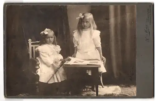 Fotografie K. Meier, Hannover, Engelbostelerdamm 130, Portrait zwei kleine Mädchen in weissen Kleidern mit Fotos