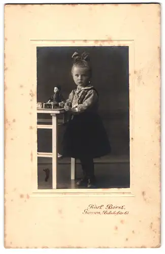 Fotografie Karl Borst, Giessen, Bahnhofstrasse 61, Portrait hübsch gekleidetes Mädchen mit Puppe am Tisch