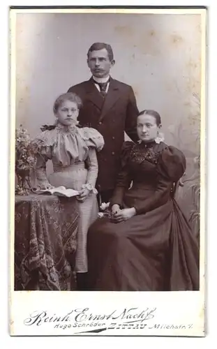 Fotografie Reinh. Ernst Nachf., Zittau, Milchstrasse 7, Portrait bürgerliches Paar mit Tochter am Tisch