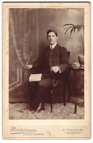 Fotografie Parisienne, Cardiff, 3, Charles St., Portrait junger Mann im Anzug mit Buch auf Stuhl sitzend