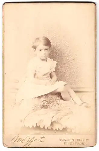 Fotografie Moffat, Edinburgh, 125, Princes St., Portrait kleines Mädchen im Kleid auf Fell sitzend