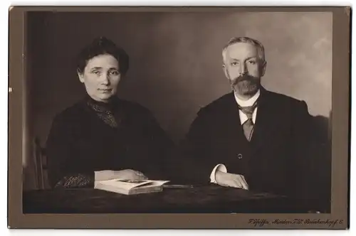 Fotografie F. Pfeiffer, Minden i /W., Brückenkopf 6, Portrait bürgerliches Paar mit Buch am Tisch sitzend