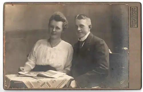 Fotografie Heinrich Petersen, Schleswig, Stadtweg 34, Portrait bürgerliches Paar mit Zeitung am Tisch sitzend