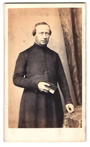Fotografie unbekannter Fotograf und Ort, Portrait Geistlicher mit Bibel an Tisch gelehnt
