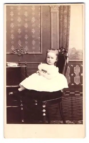 Fotografie J. Petersen, Kiöbenhavn, Kleines Mädchen in weissem Kleid sitzt auf gepolstertem Stuhl