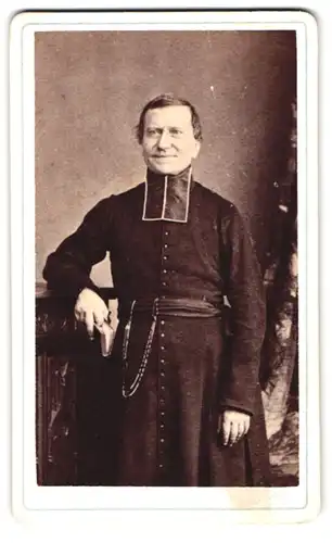 Fotografie Th. Schahl, Dijon, 29, Rue Chabot-Charny, Portrait charmanter Priester im Talar an einem Stuhl stehend